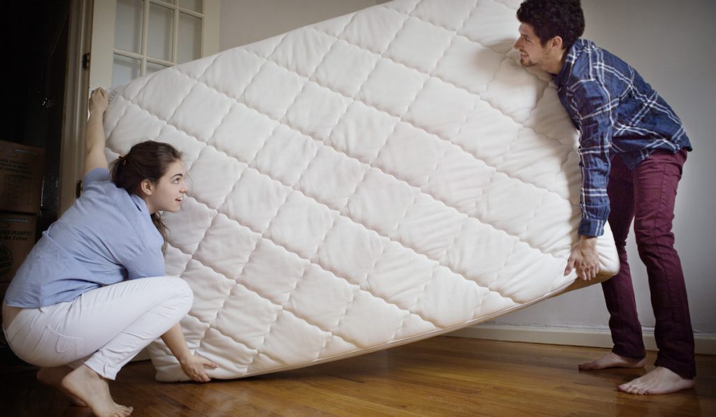 Couple Carrying Mattress In Room
