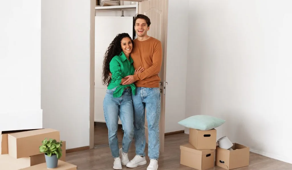 Happy couple standing near the door of their new apartment with cardboard boxes on the floor