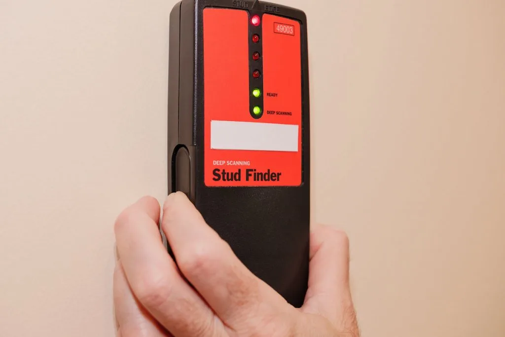 Male carpenter using electronic stud finder to locate interior wall stud.
