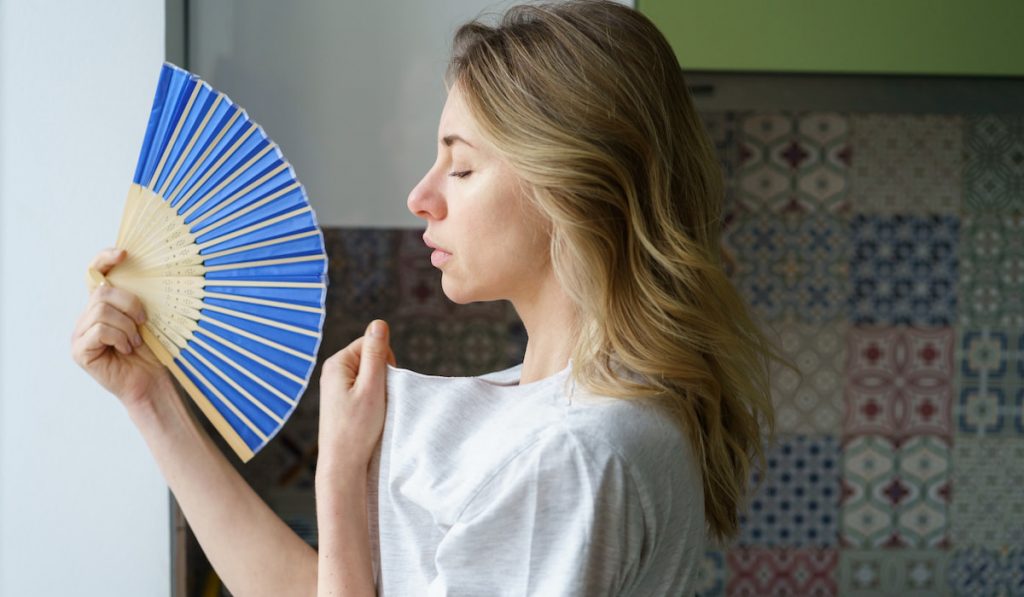 Side view of tired woman in t-shirt using wave fan suffer from heat sweating