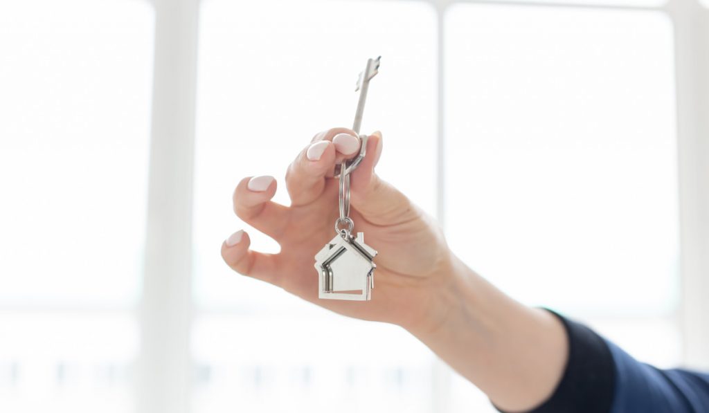 woman holding apartment key and house shaped keychain in new apartment