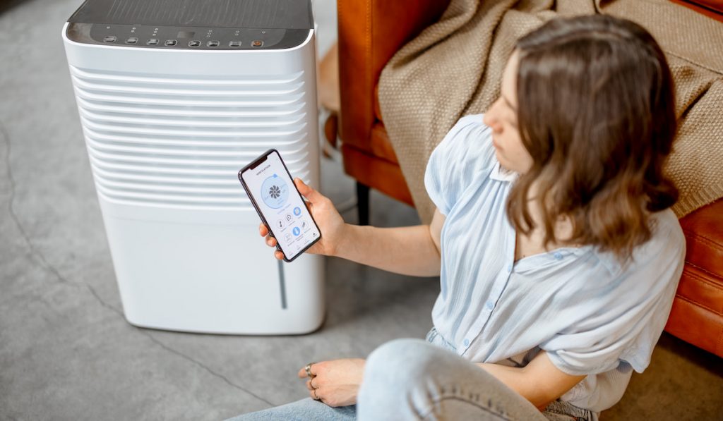 woman sitting near air Dehumidifier in the sofa and checking the app using her phone