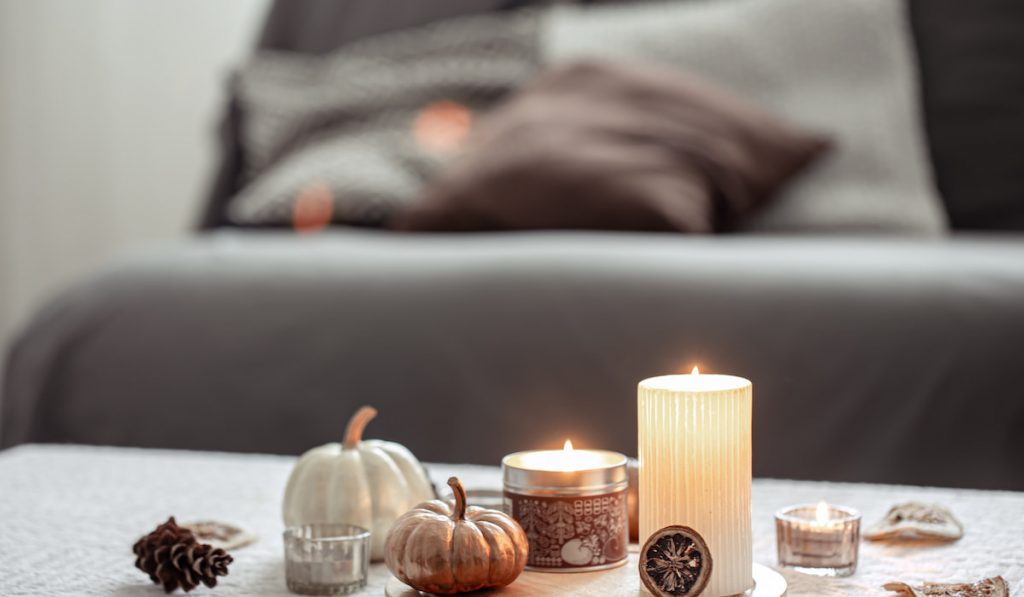 Cozy last minute candles and pumpkins on blurred background in the interior of the room.

