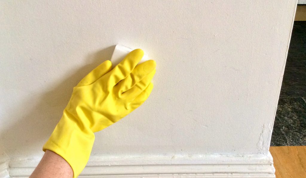 Woman’s hand in yellow glove cleaning white wall